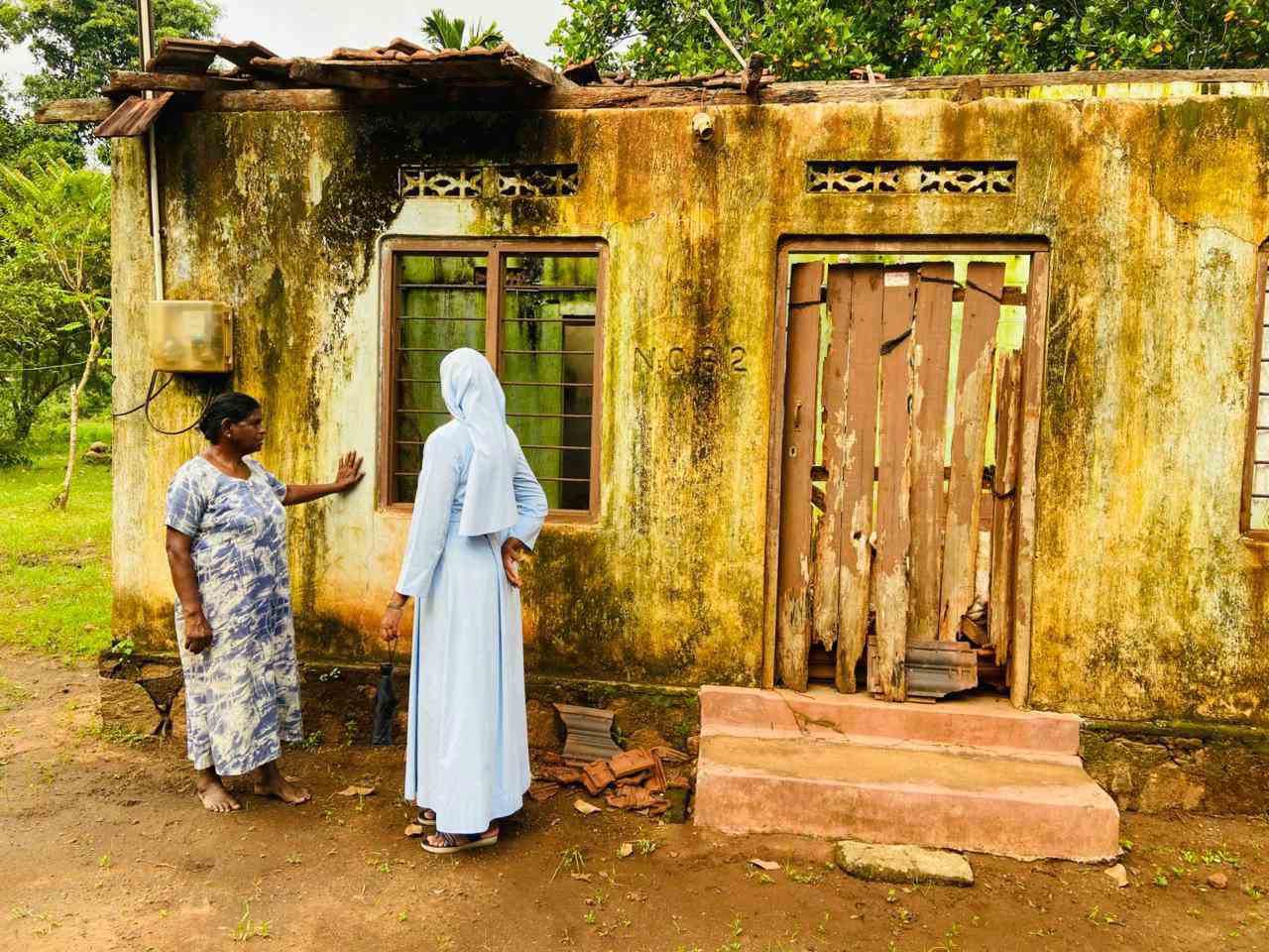 Schwester in Sri Lanka vor einer Frau mit ihrem Haus, das ganz gelb ist vom Schlamm.